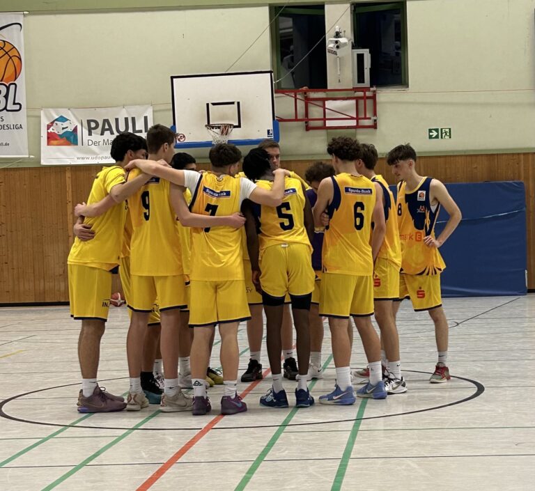 Eine Basketballmannschaft in gelben Trikots versammelt sich im Kreis, engagiert und fokussiert.