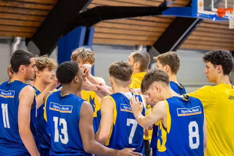 Team in blauen Trikots beim motivierten Gruppenhandschlag auf dem Basketballplatz.