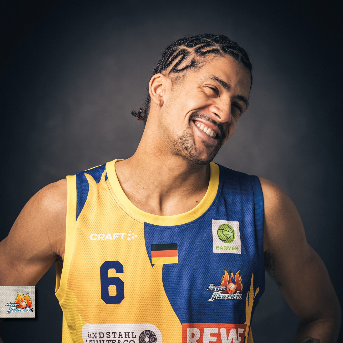 Lächelnder Basketballspieler im gelben Trikot mit Zopf, Logo und Nummer 6, vor dunklem Hintergrund.