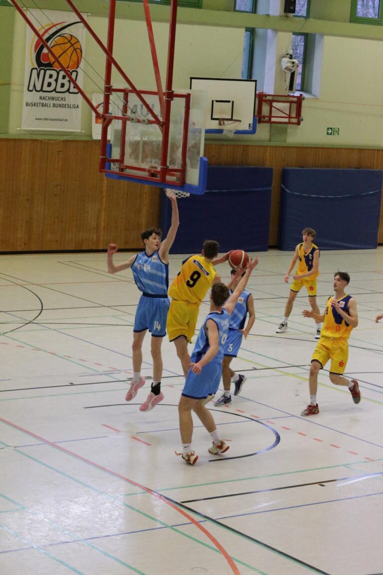 Ein Basketballspiel in einer Sporthalle zeigt Spieler in gelben und blauen Trikots in Aktion.