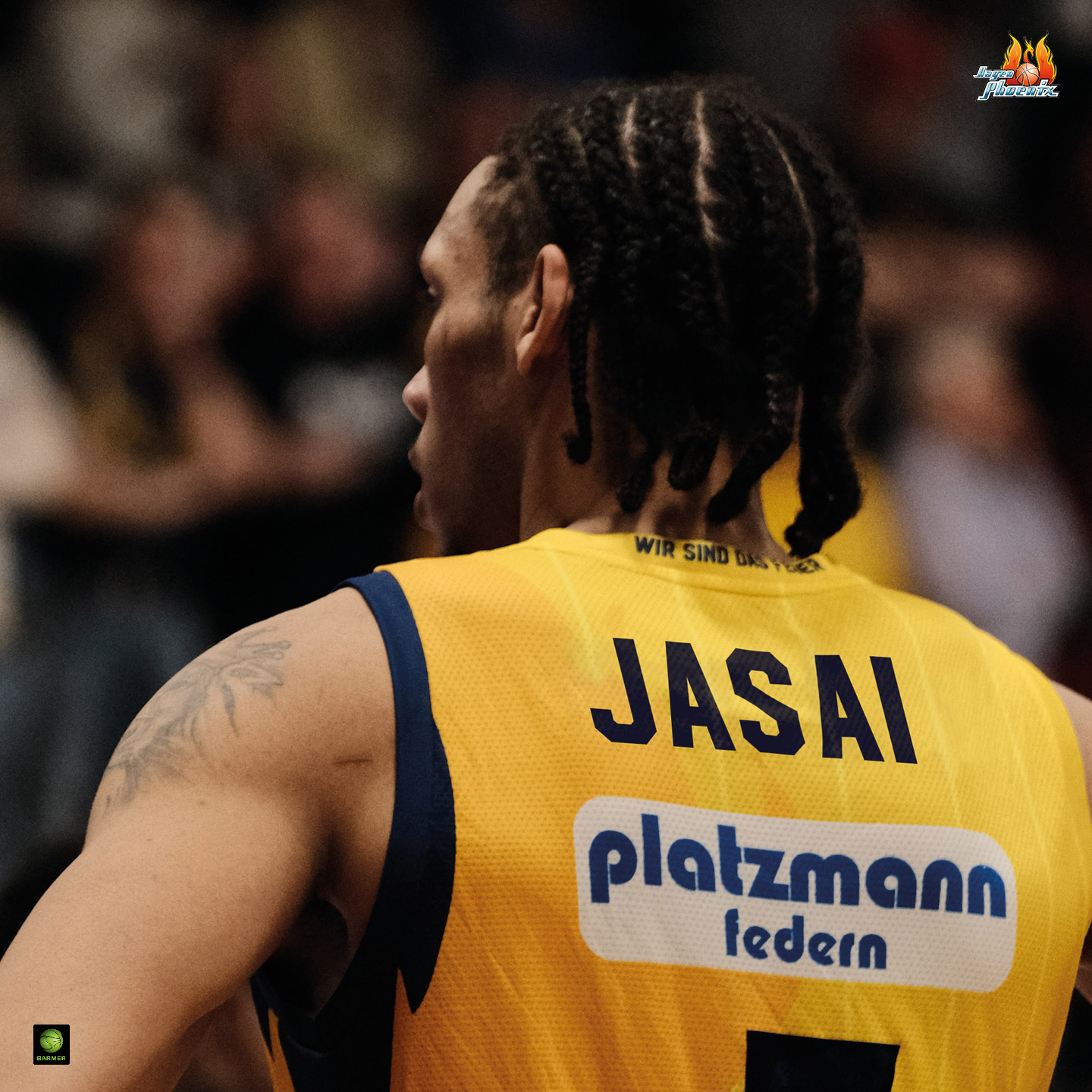 Basketballspieler mit Zopf, gelbes Trikot, konzentrierter Ausdruck, muskulös, tätowierter Arm.