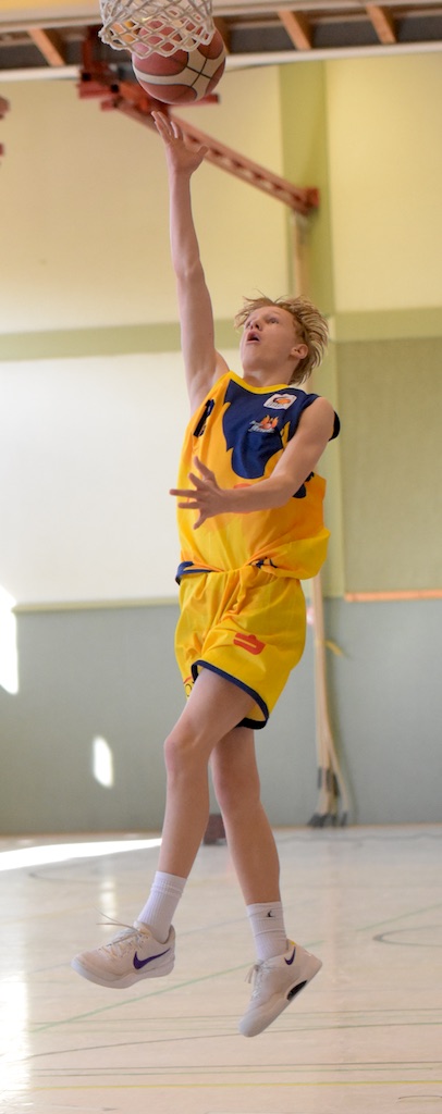 Ein junger Basketballspieler in gelbem Trikot beim Korbleger, konzentrierter Ausdruck.