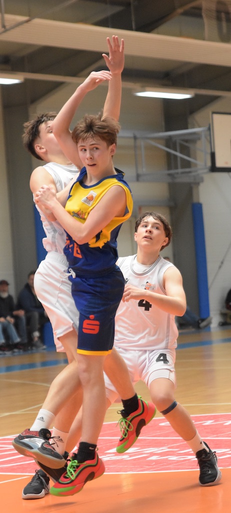 Ein Basketballspieler im blau-gelben Trikot, springend, weicht einem verteidigenden Spieler aus.
