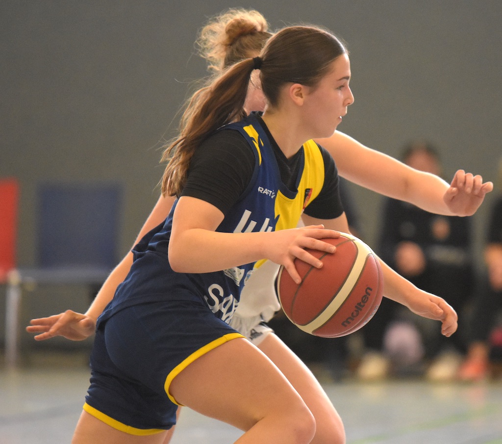 Basketballspielerin im blauen Trikot, konzentriert, dribbelt den Ball, gegnerische Abwehr.