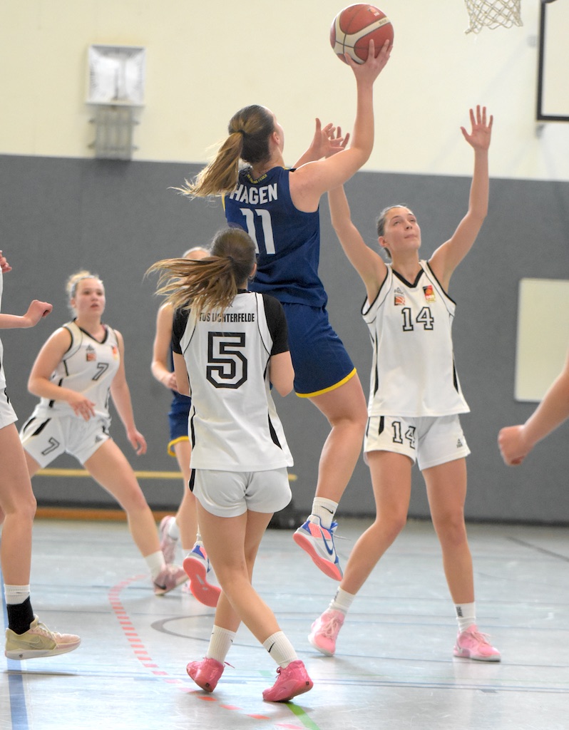 Eine Basketballspielerin in blauem Trikot springt, während andere zusehen.