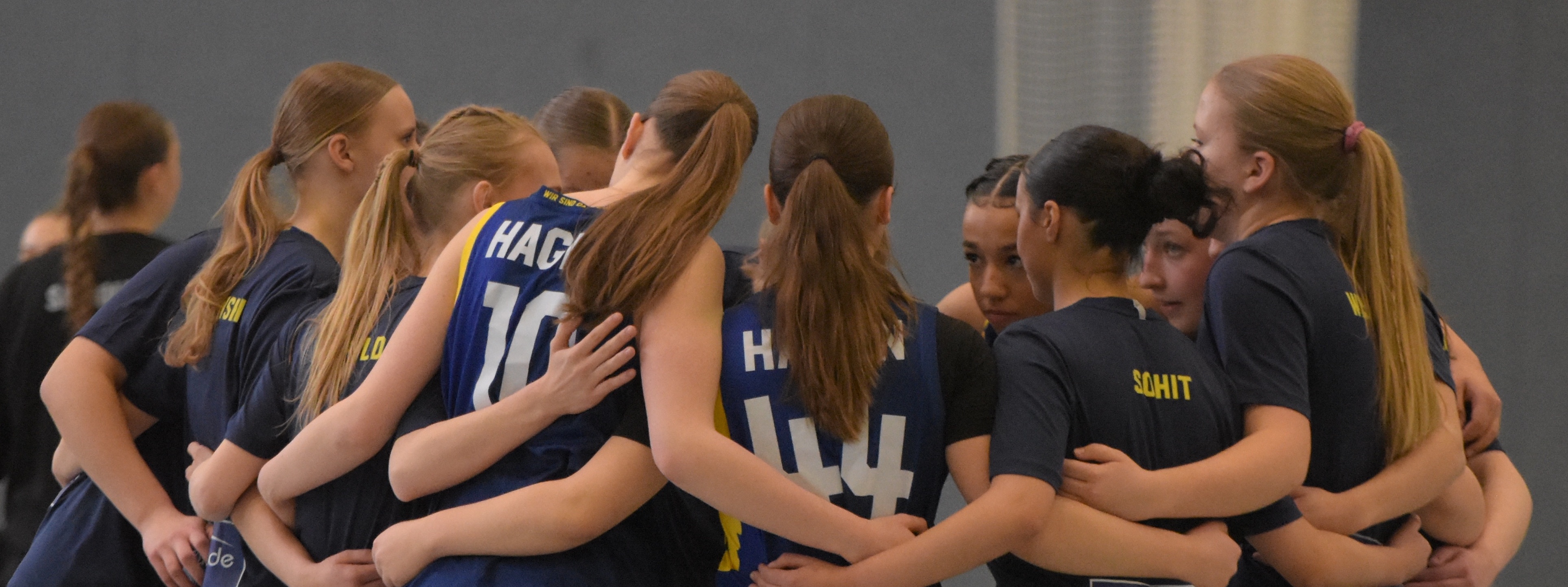 Eine Gruppe junger Volleyballspielerinnen umarmt sich konzentriert im Kreis.