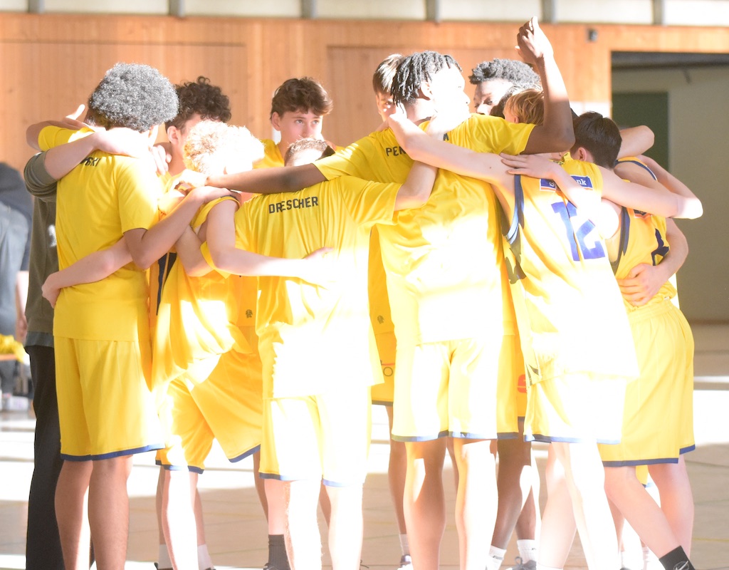 Eine Gruppe von Basketballspielern in gelben Trikots umarmt sich in der Mitte des Spielfelds.