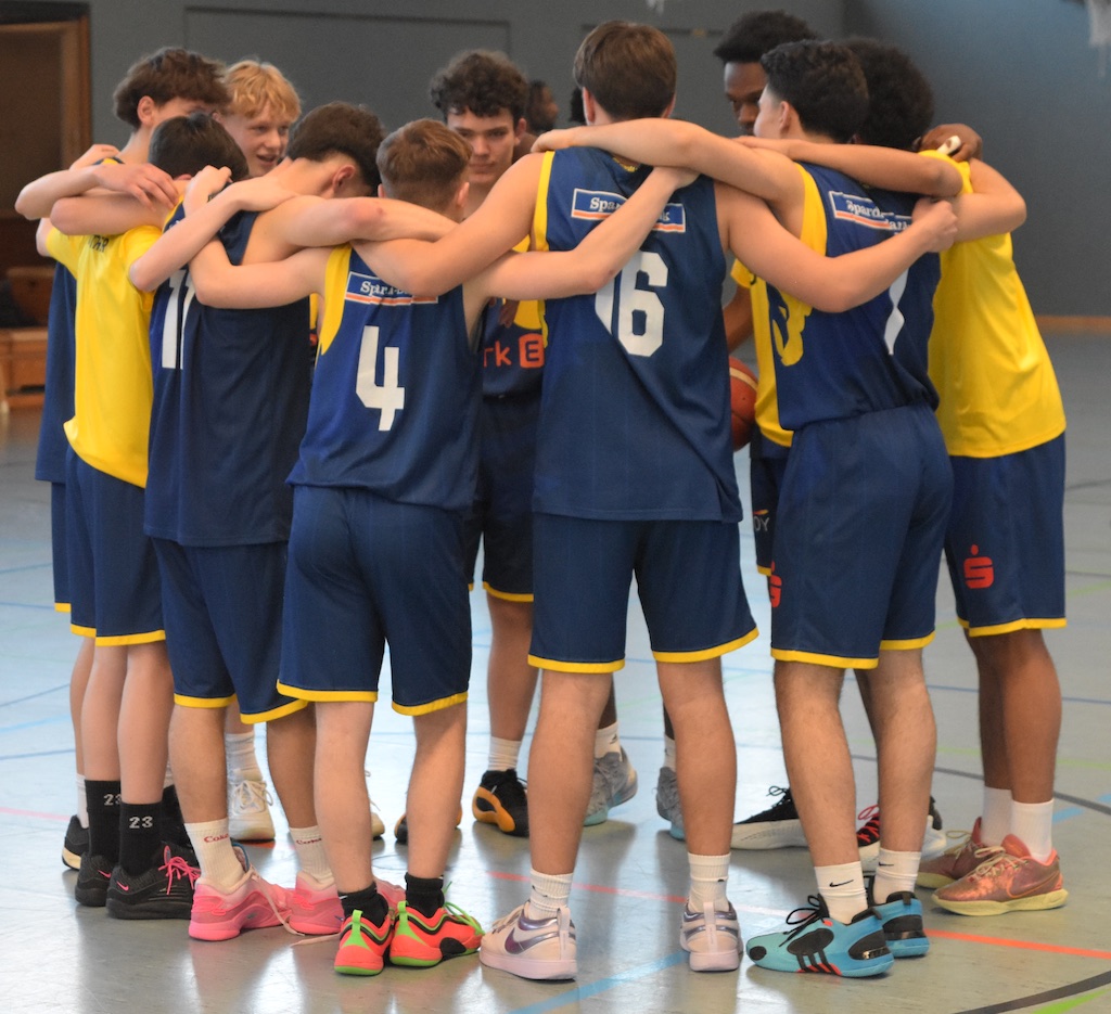 Mehrere Basketballspieler in blauen Trikots umarmen sich; Gruppenumarmung vor dem Spiel.