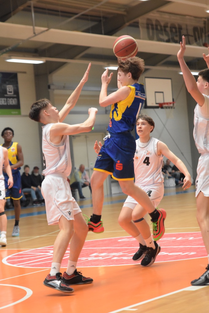 Junger Basketballspieler in der Luft mit Ball, blau-gelbes Trikot, dynamische Spielszenen.
