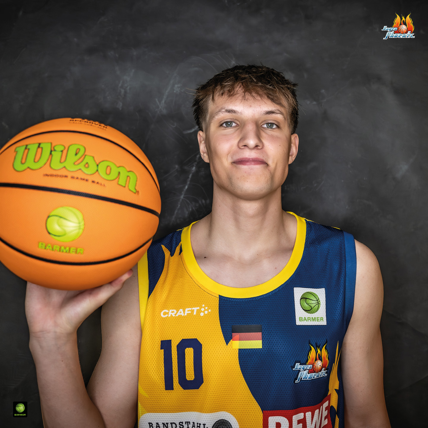 Junger Mann im Basketballtrikot hält lächelnd einen orangefarbenen Basketball.