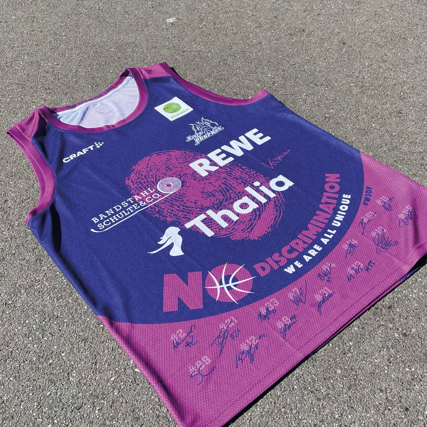 Ein Trikot in Lila und Blau auf Asphalt mit Unterschriften und Logos, inklusive "NO DISCRIMINATION".