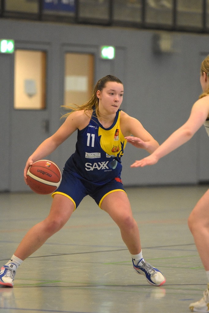 Eine Basketballspielerin konzentriert sich auf Dribbling. Sie trägt ein blau-gelbes Trikot.