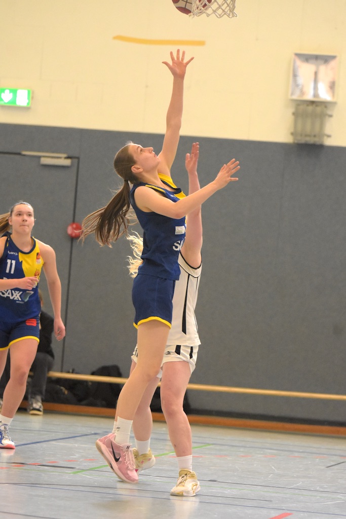 Basketballspielerin im blauen Trikot macht einen Korbleger, konzentriert, Sporthalle.