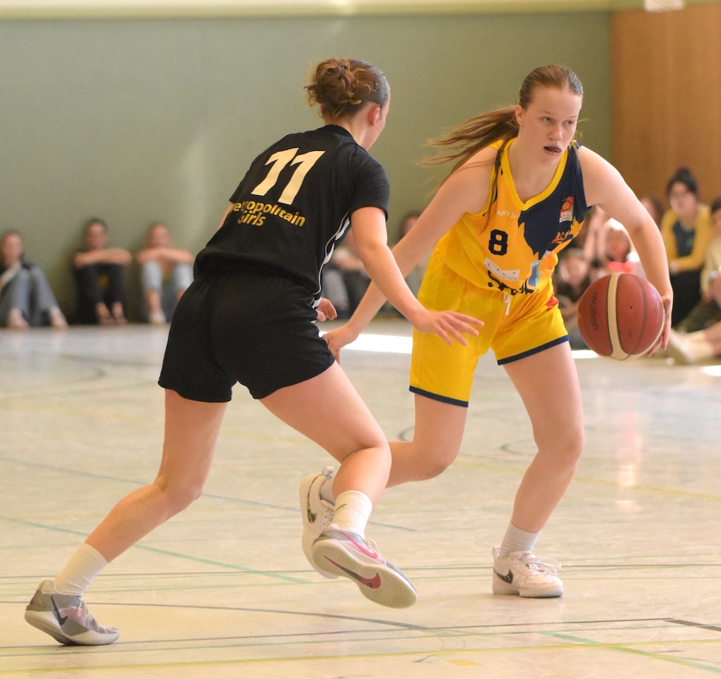Zwei Basketballspielerinnen, konzentriert im Spiel. Eine trägt ein gelbes, die andere ein schwarzes Trikot.