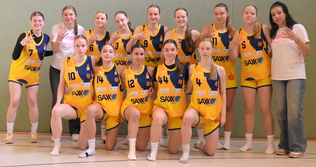 Eine Frauen-Basketballmannschaft posiert lächelnd in gelben Trikots und Sportsocken.