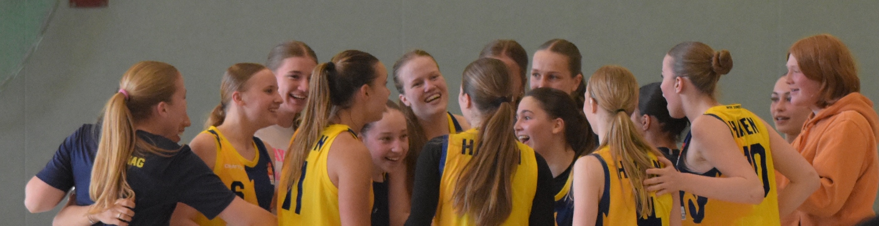 Mehrere Frauen im gelben Basketball-Trikots lächelnd in einem Kreis.