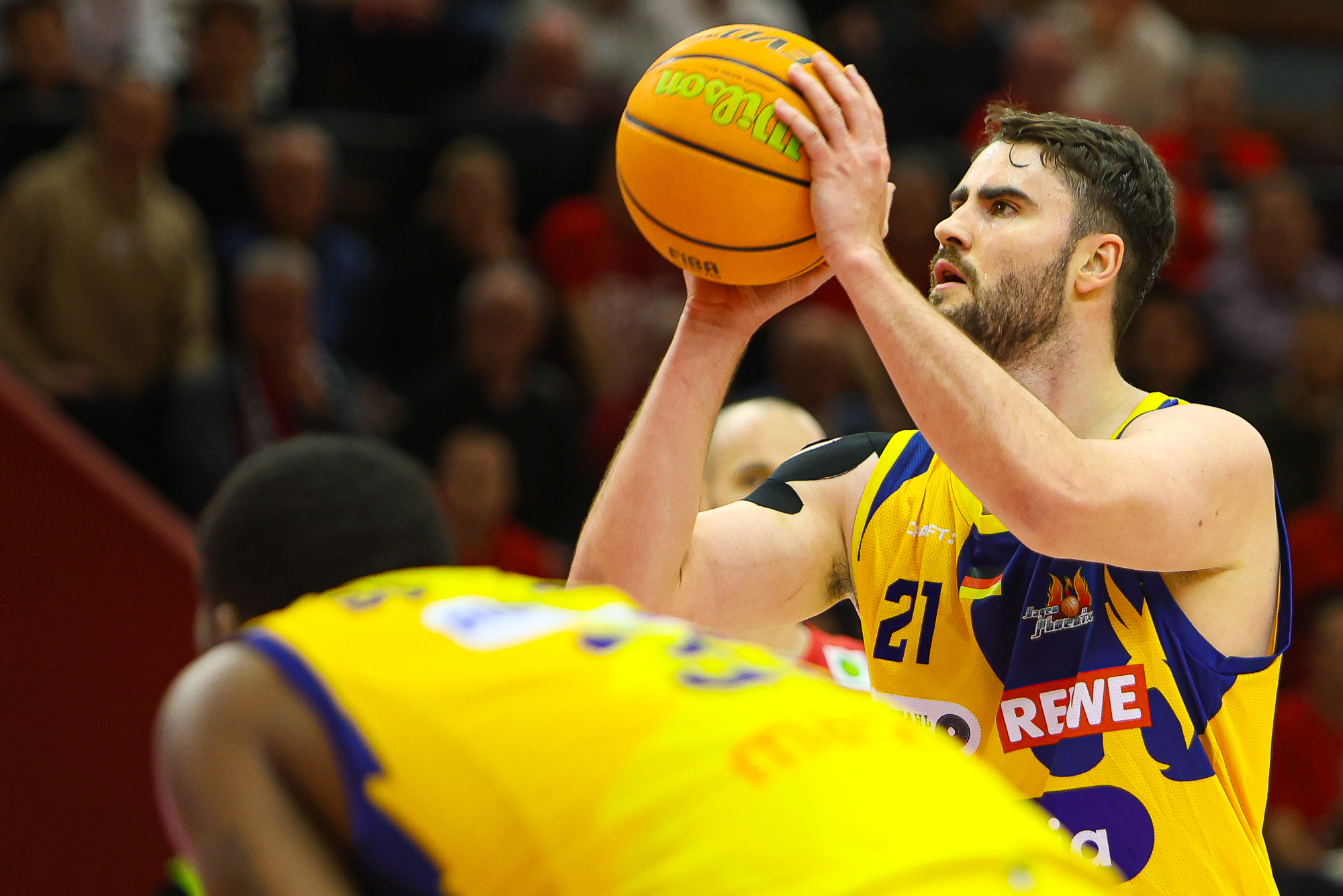 Ein Basketballspieler im gelb-blauen Trikot beim Freiwurf, konzentrierter Ausdruck.