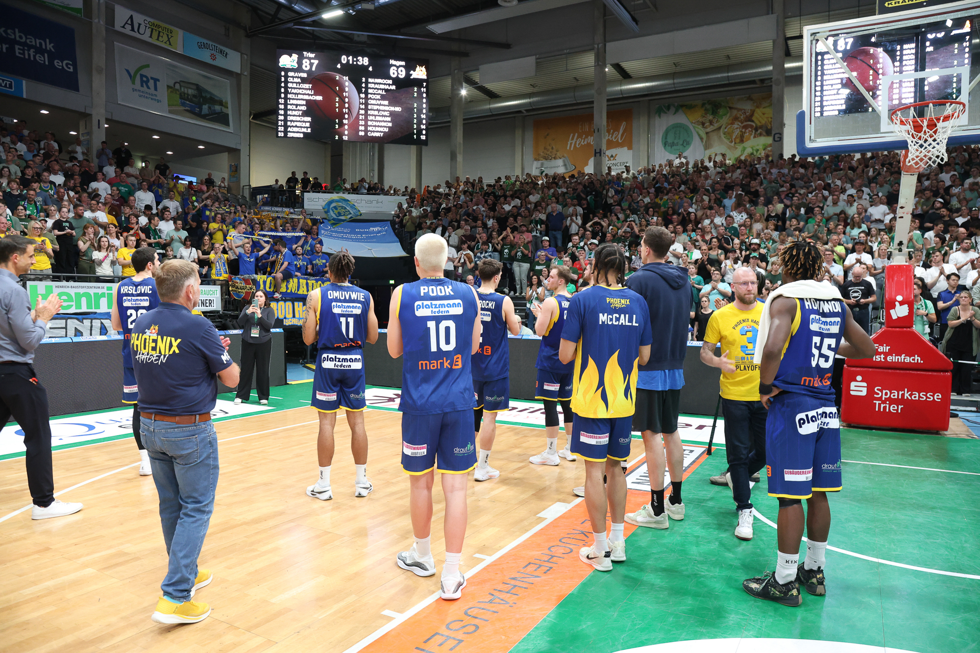 Ein Basketballteam in blauen Trikots feiert auf dem Spielfeld, umgeben von jubelnder Menge.