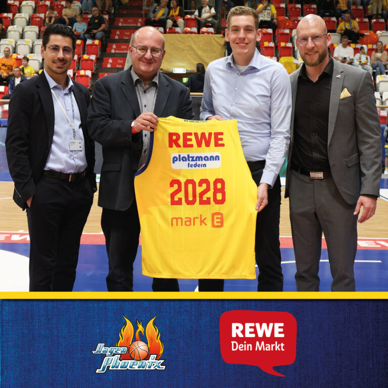 Zwei Männer, ein dunkler Anzug, einer ein gelbes Basketballtrikot. Alle lächeln freundlich.