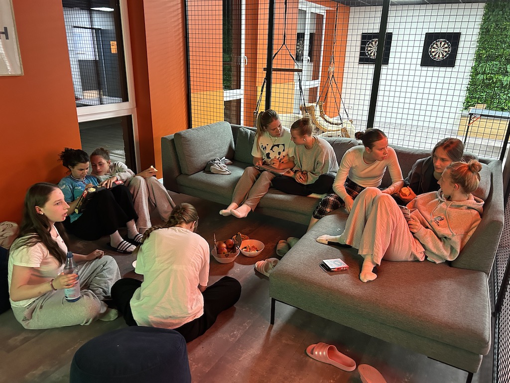 Gruppe von jungen Frauen in lockerer Kleidung, lachend und plaudernd auf Sofas in einem Freizeitraum.