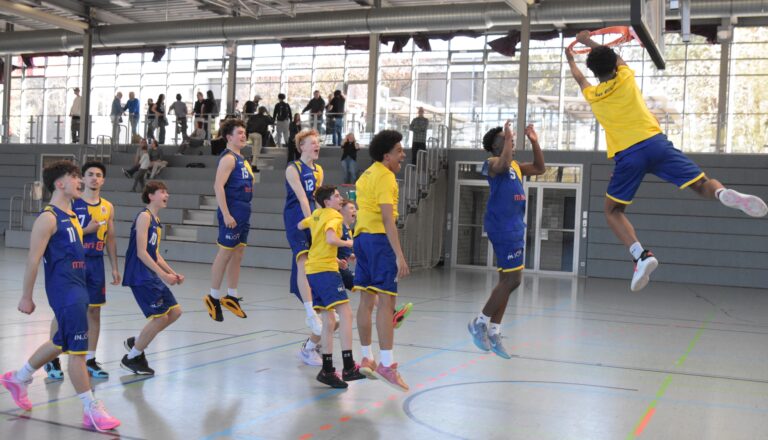 Eine Gruppe von Jugendlichen spielt Basketball in einer Turnhalle, ein Spieler dunkt in den Korb.