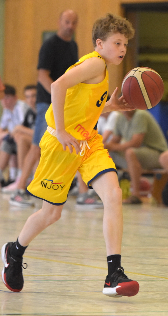 Junger Basketballspieler in gelbem Trikot dribbelt fokussiert einen Ball auf dem Spielfeld.