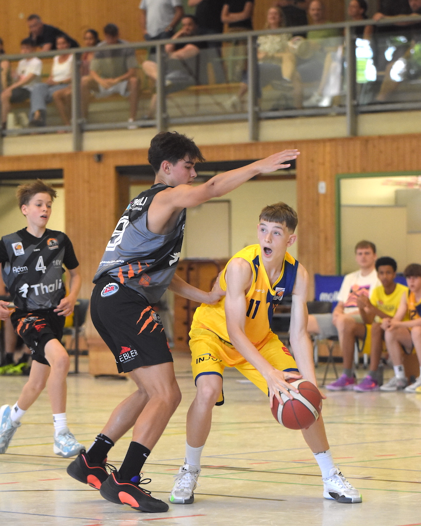 Zwei Jugendbasketballspieler in Aktion; Gelbes Trikot entschlossen, graues Trikot verteidigend.