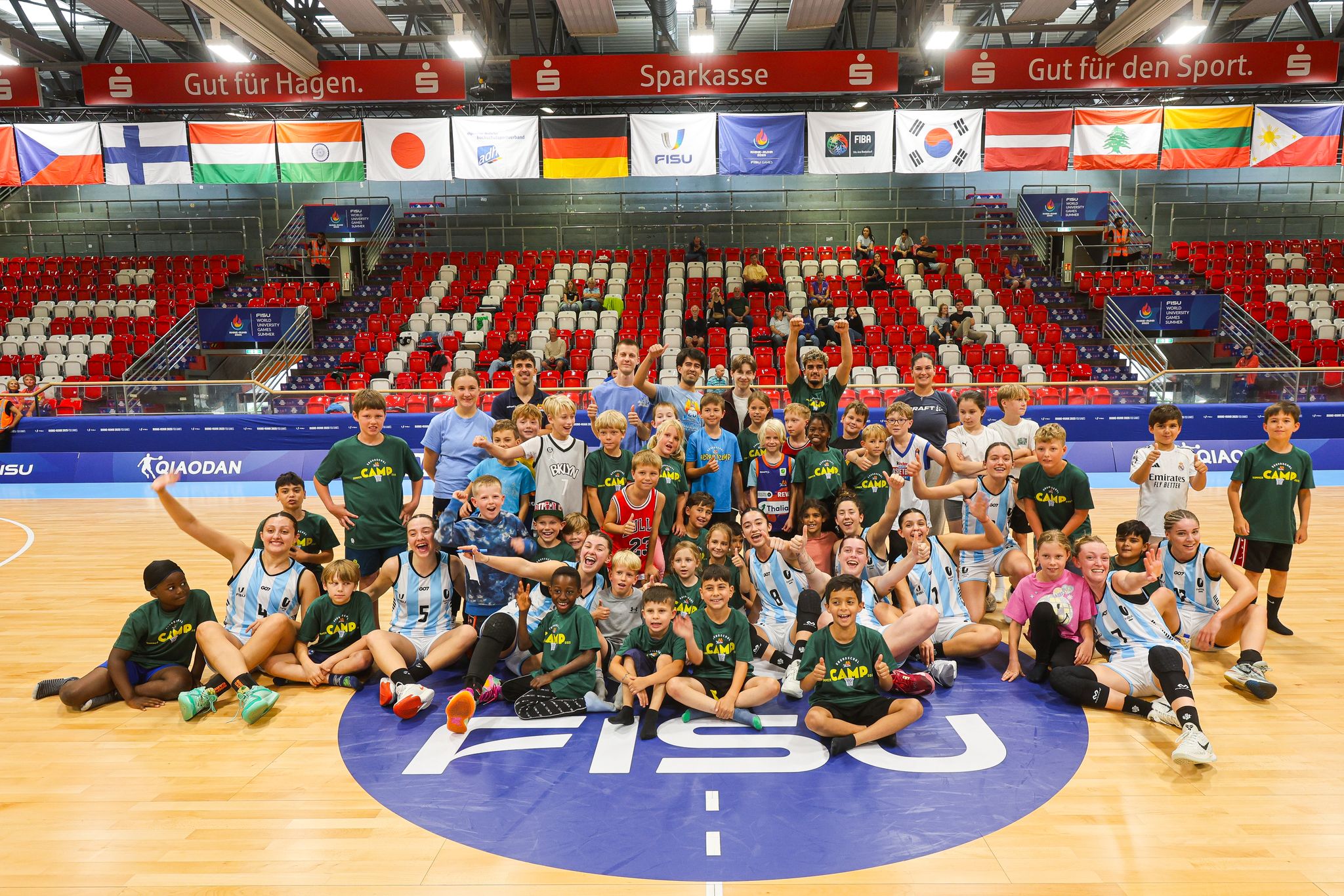 Eine Gruppe von Kindern und Erwachsenen lächelt in einer Sporthalle auf einem Basketballfeld.