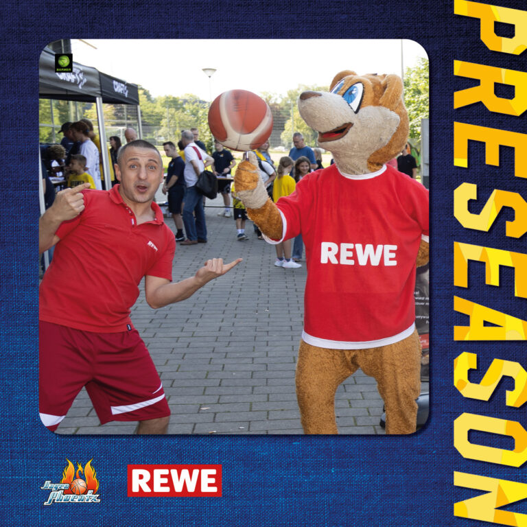 Eine Person in Rot und ein Maskottchen mit Basketball lächeln für die Kamera.