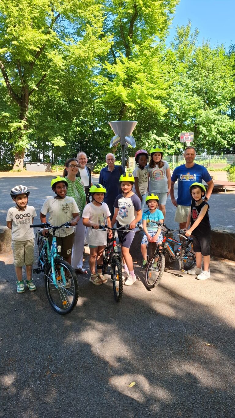 Eine Gruppe von Kindern mit Helmen posiert lächelnd mit Fahrrädern an einem sonnigen Tag.