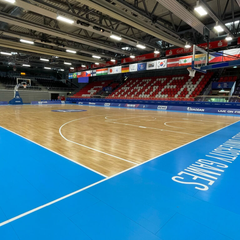 Hölzerner Basketballplatz mit blauen Rändern, leeren Tribünen und Deckenbannern in einer Sporthalle.