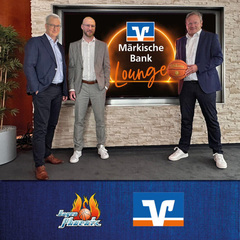 Drei Männer in Anzügen posieren lächelnd mit einem Basketball vor einem Logo.