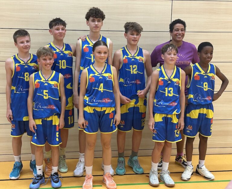 Neun junge Basketballspieler in blau-gelben Trikots stehen lächelnd da.