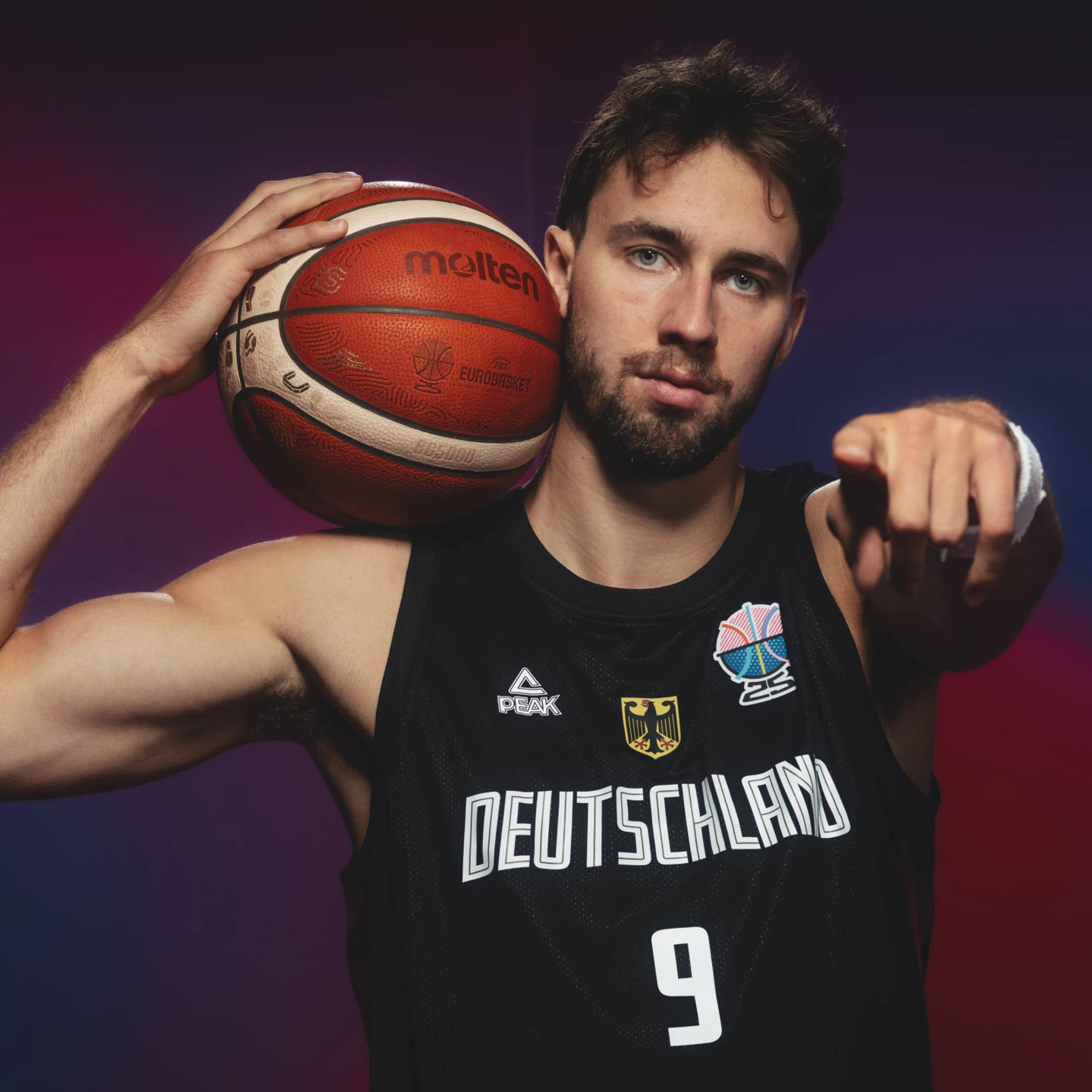 Ein Basketballspieler im Deutschland-Trikot hält einen Ball und zeigt entschlossen.