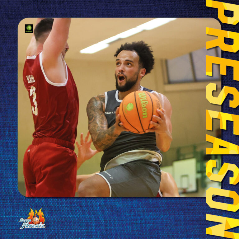 Ein Basketballspieler versucht mit konzentriertem Gesichtsausdruck zu punkten, während ein Gegner in rotem Trikot verteidigt.