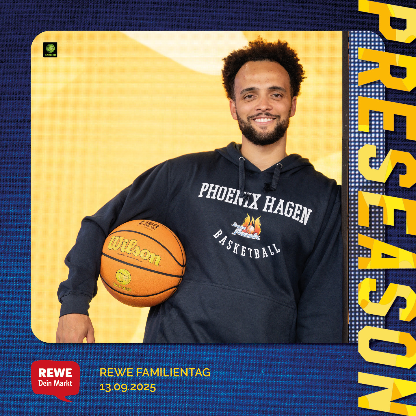 Ein Mann mit lockigem Haar lächelt, hält einen Basketball im Arm, trägt ein dunkles Hoodie.