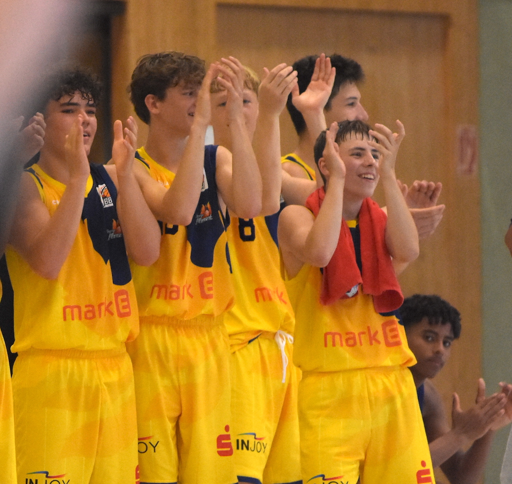 Eine Gruppe von jungen Basketballspielern in gelben Trikots applaudiert gespannt.