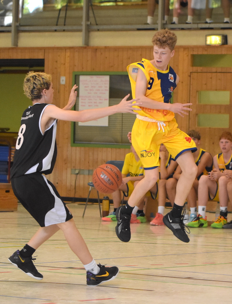 Zwei jugendliche Basketballspieler in Aktion, einer in gelbem Trikot springt.