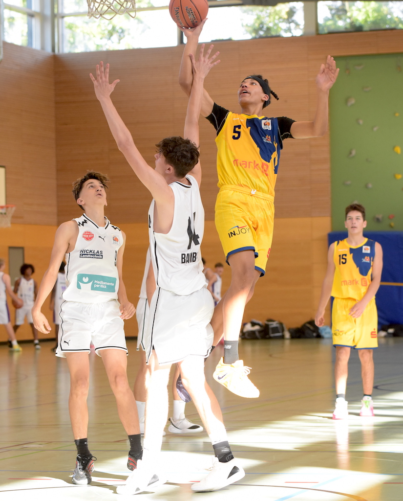 Ein Basketballspieler im gelben Trikot springt zum Korb, konzentriert.