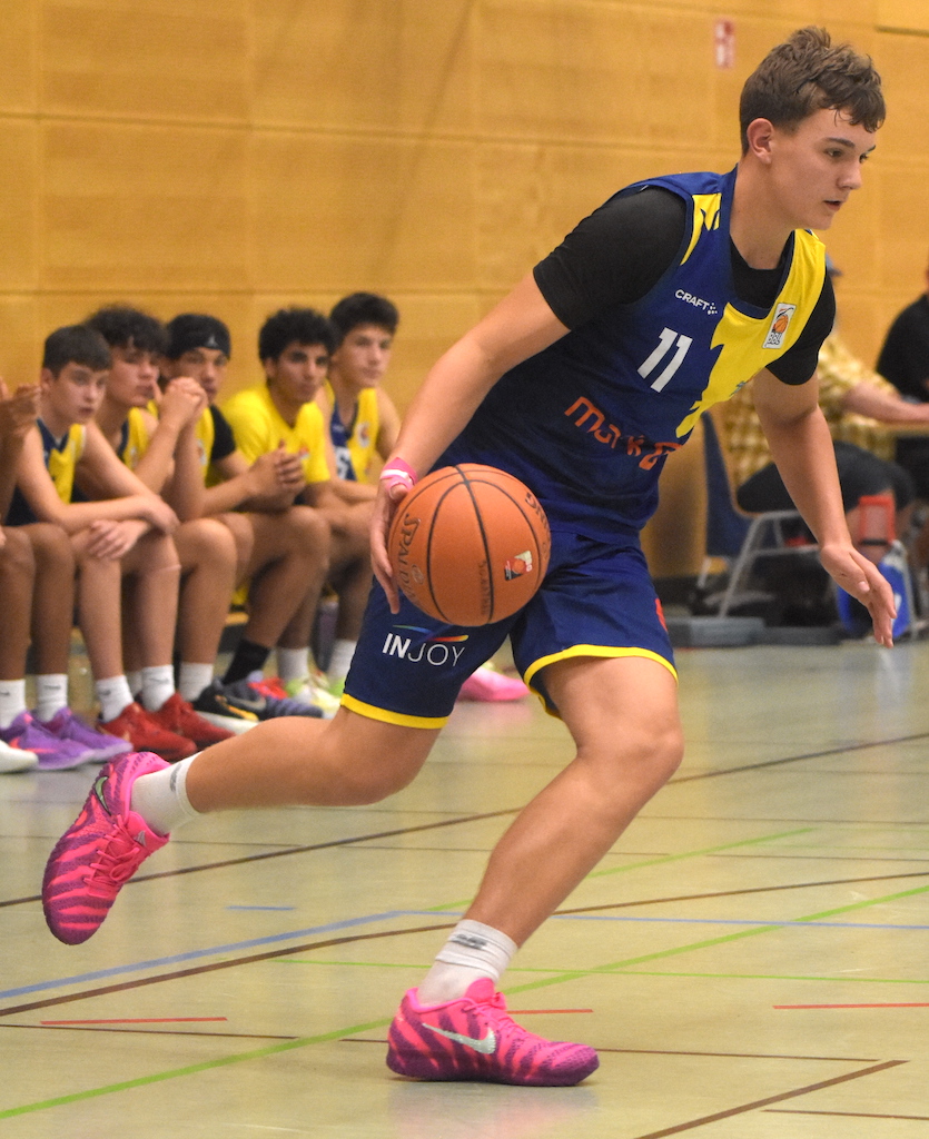 Ein jugendlicher Basketballspieler in blauer Uniform dribbelt den Ball energisch.