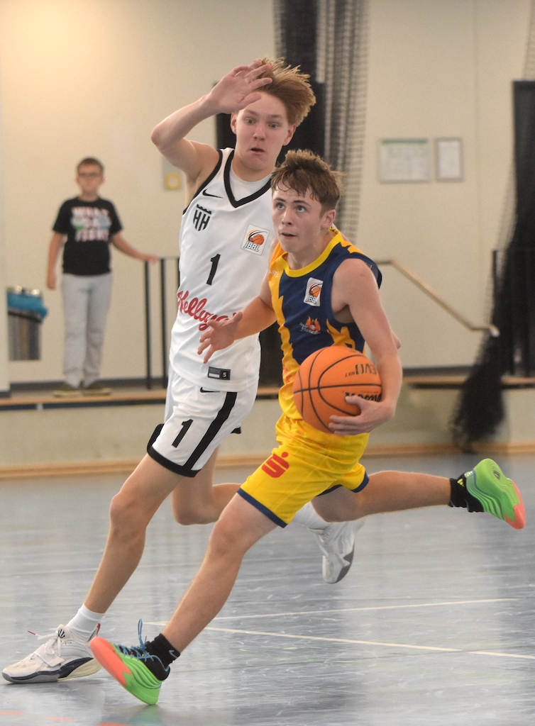 Ein jugendlicher Basketballspieler im gelben Trikot dribbelt mit ernster Miene.