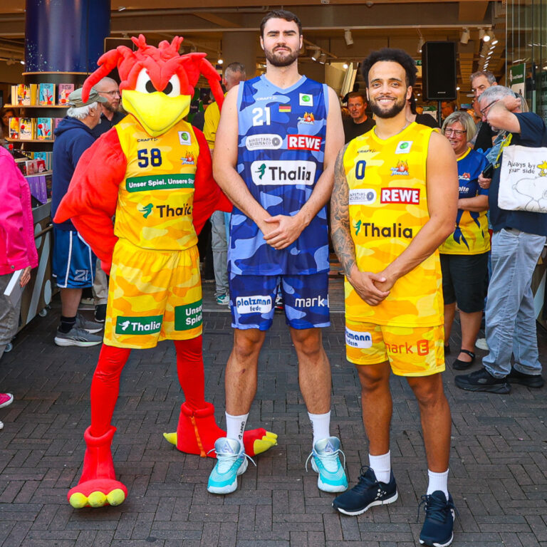 Drei Menschen, zwei Basketballspieler in gelben Trikots, lachen fröhlich.