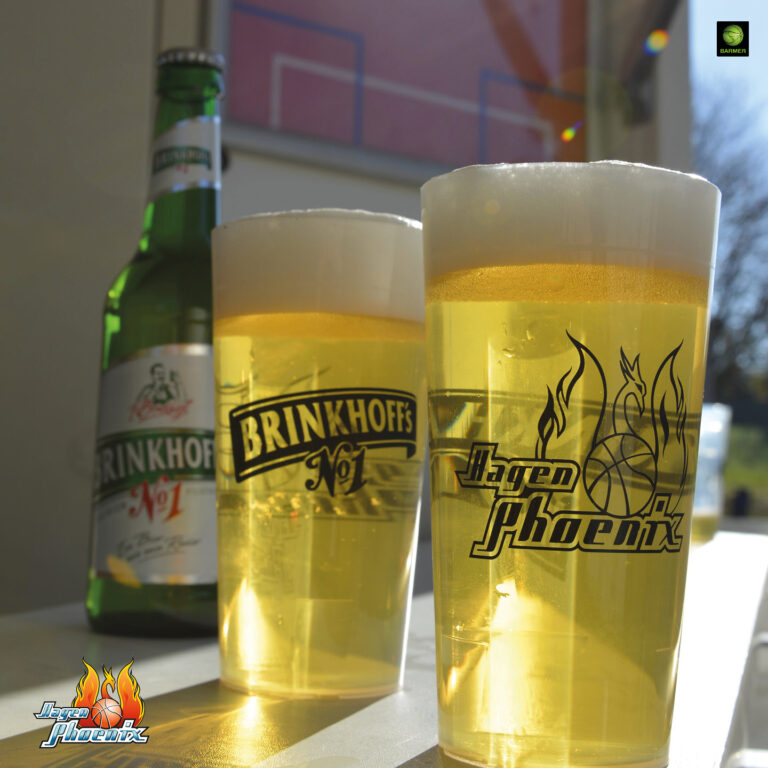 Zwei voll gefüllte Gläser Bier vor einer Flasche auf einem Tisch in der Sonne.