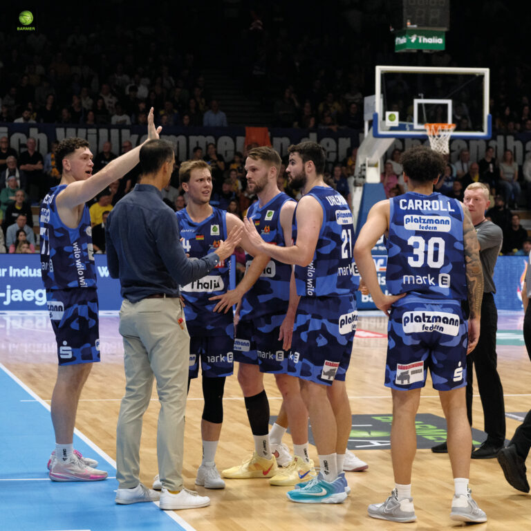 Eine Basketballmannschaft in blauen Trikots versammelt sich zur Beratung.