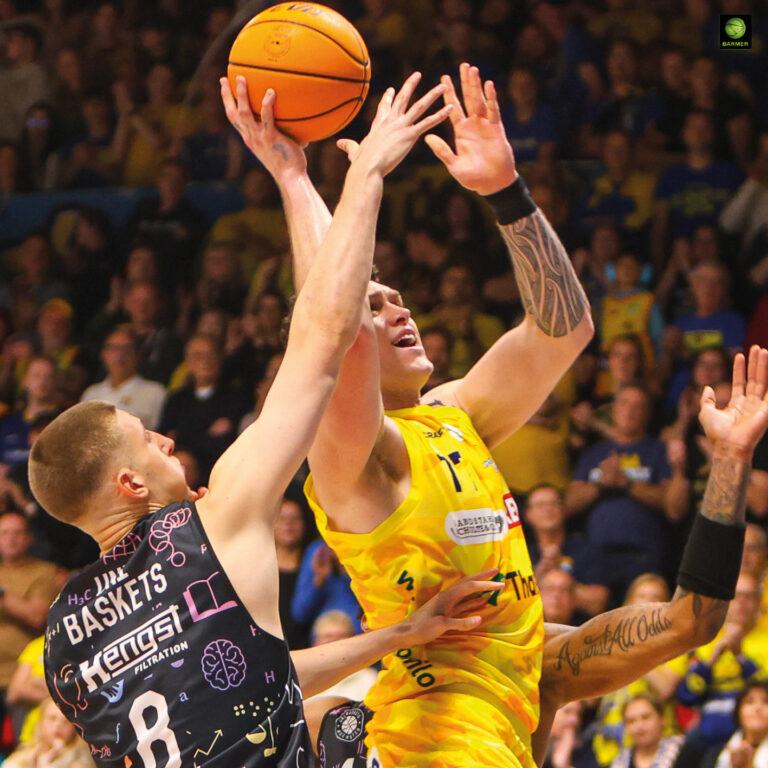 Zwei Basketballspieler kämpfen fokussiert um den Ball, einer im gelben Trikot springend