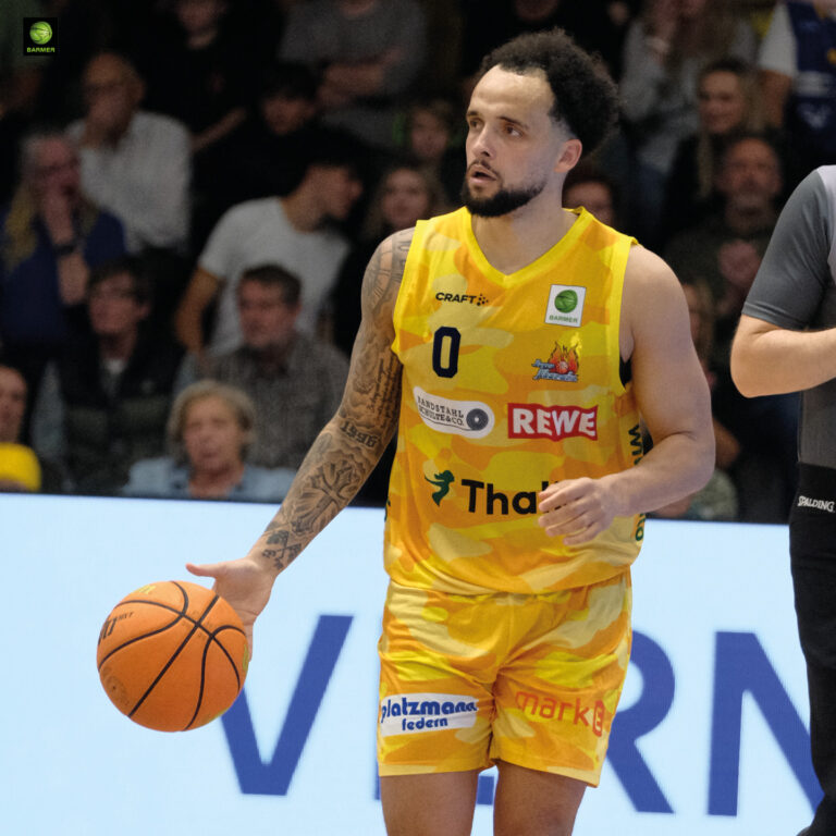 Ein Basketballspieler mit gelbem Trikot und ruhigem Gesichtsausdruck hält den Ball
