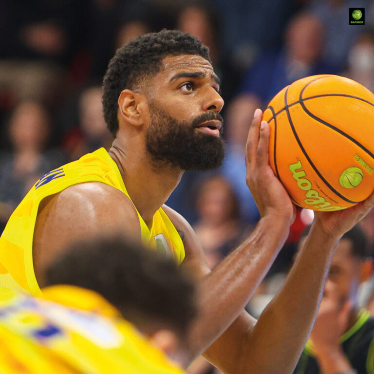 Ein Basketballspieler mit buschigem Bart und gelbem Trikot konzentriert beim Freiwurf
