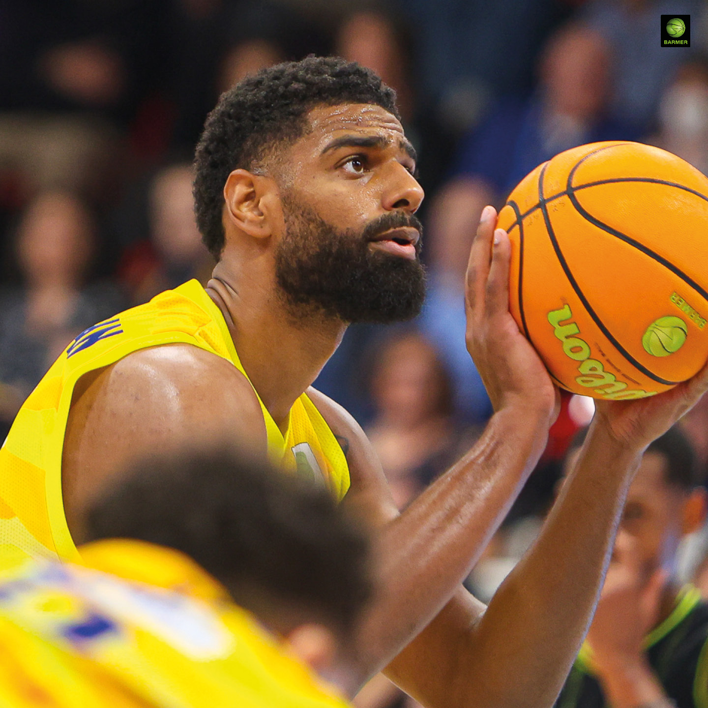 Ein Basketballspieler mit buschigem Bart und gelbem Trikot konzentriert beim Freiwurf