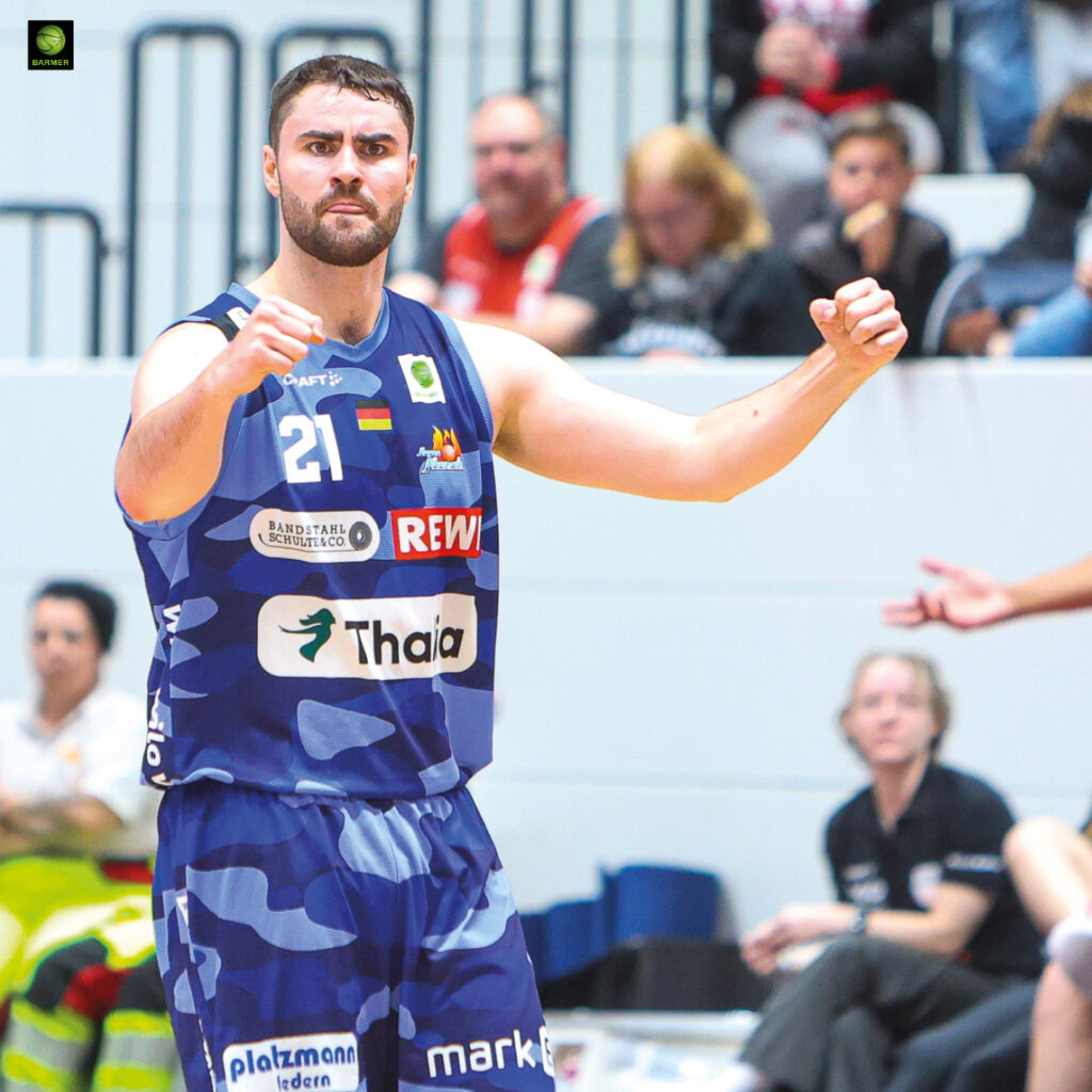 Ein Basketballspieler im blauen Trikot jubelt kraftvoll mit erhobenen Fäusten