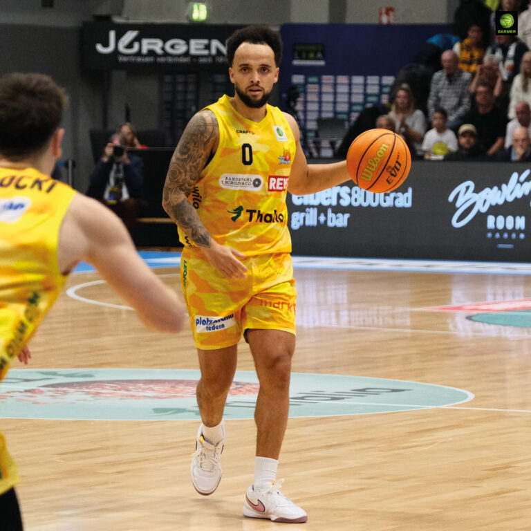 Ein Basketballspieler in gelbem Trikot dribbelt konzentriert über das Spielfeld